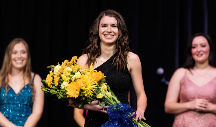 Three women with one in center focus smiling at the camera with flowers