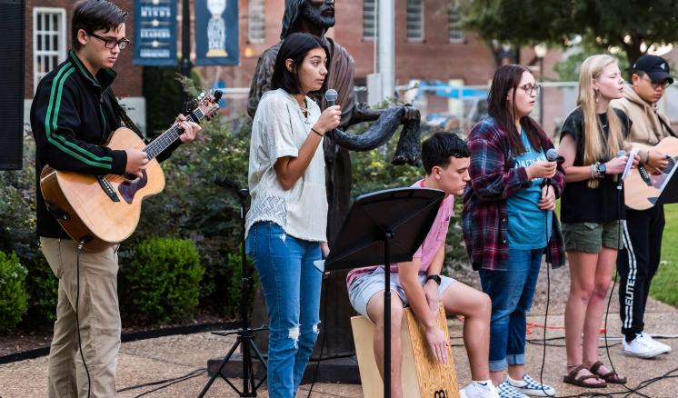 A group of men and women with instruments and microphones outside in front of Jesus statue