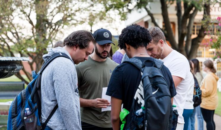 Group of men in a circle with their heads down praying outside