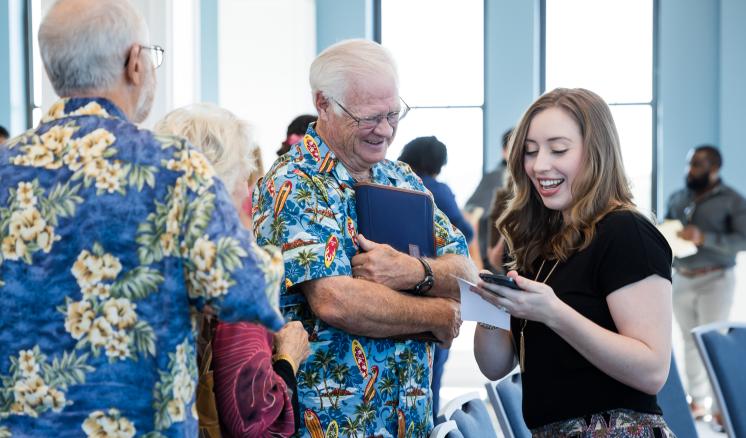 A man and a woman smiling down at her phone with another man in the foreground