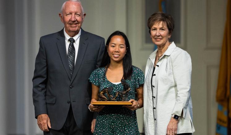 Two women and one man in a chapel with the middle person holding an award