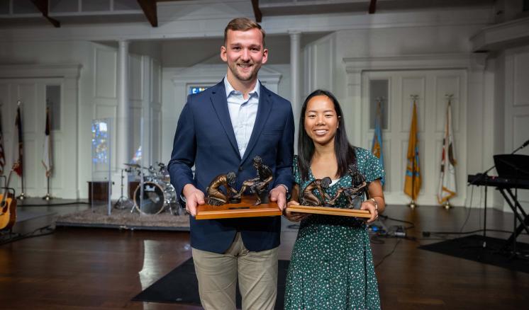 A man and a woman smiling at the camera on a stage holding awards