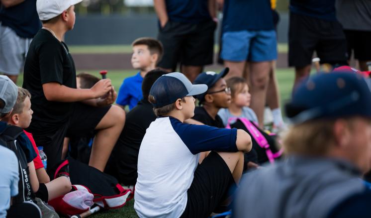 A group of kids sitting on the floor of the baseball field