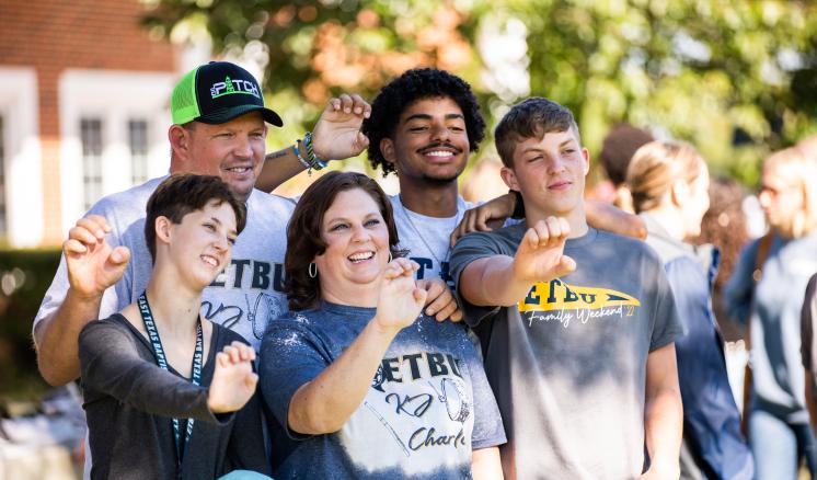 Family smiling past the camera on the right holding up the tiger paw outside 