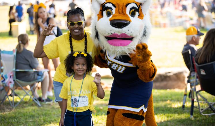 2022_family_weekend_img_2 A little girl and a grown woman holding up the tiger paw with tiger mascot
