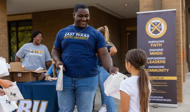 A man smiling at a little girl giving her a bag with other people in the background