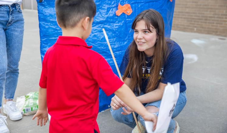 A woman down at a little boys level with a blue tarp with fish cutouts in the background