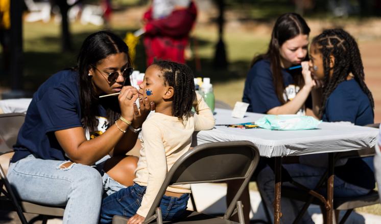 Two female students face paiting two little kids at a table