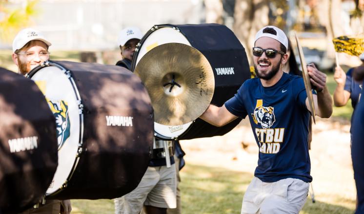 A man holding cymbals apart smiling with drums around him