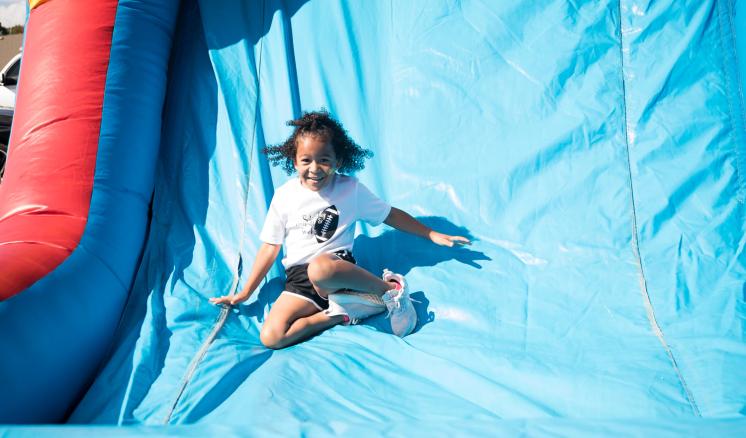 A little girl smiling at the camera going down a bouncy house slide