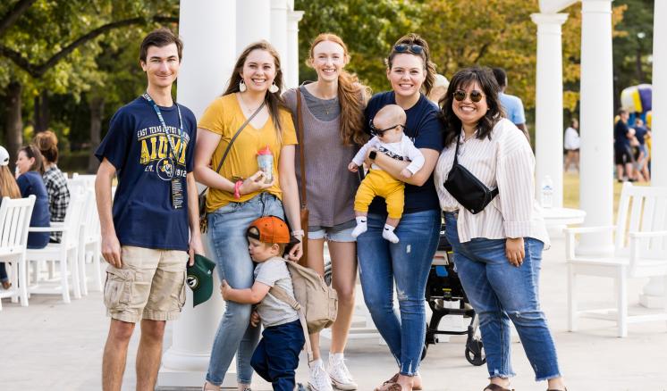 A group of a men and women with kids smiling at the camera outdoors.