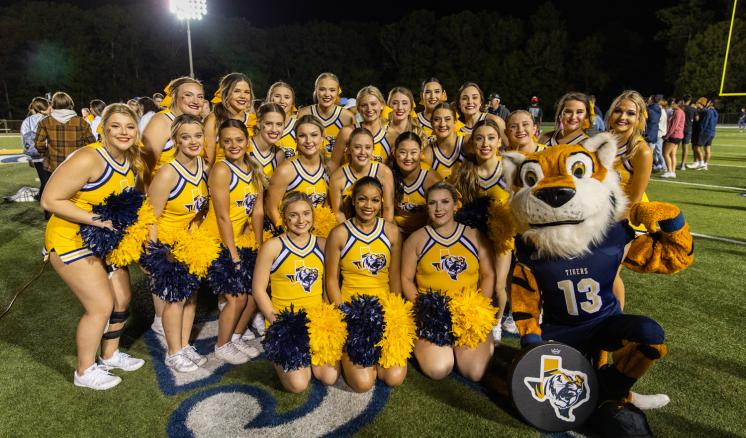 A group of cheerleaders smiling at the camera with the tiger mascot at the football field