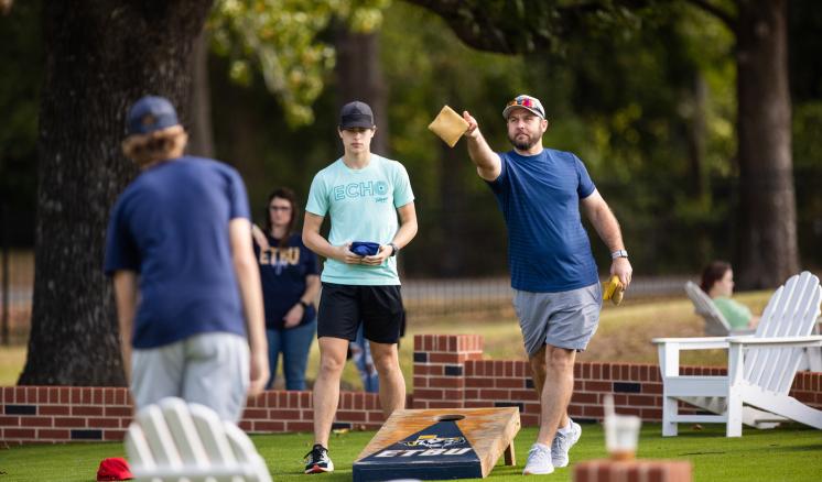 Three men playing cornhole outside