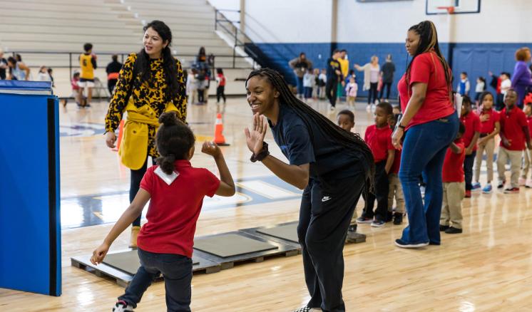 A woman giving a high five to a little boy in the gym with other people in the background