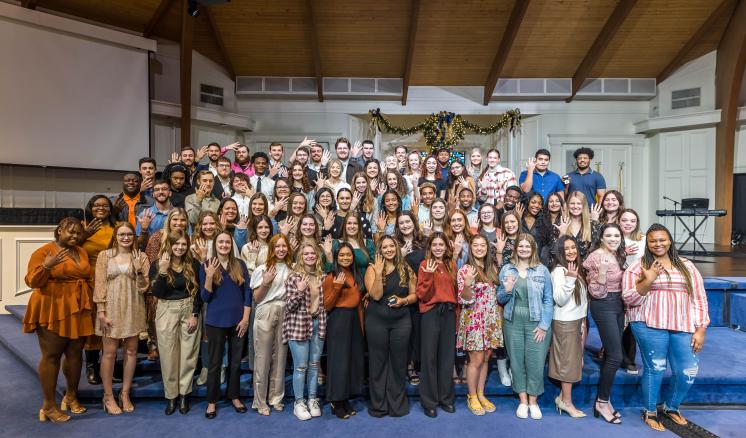 Group photo in a chapel holding their hands out to show rings on their fingers