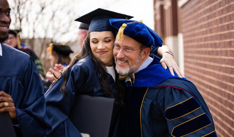 A man and a women embracing each other smiling in their graduation regalia 