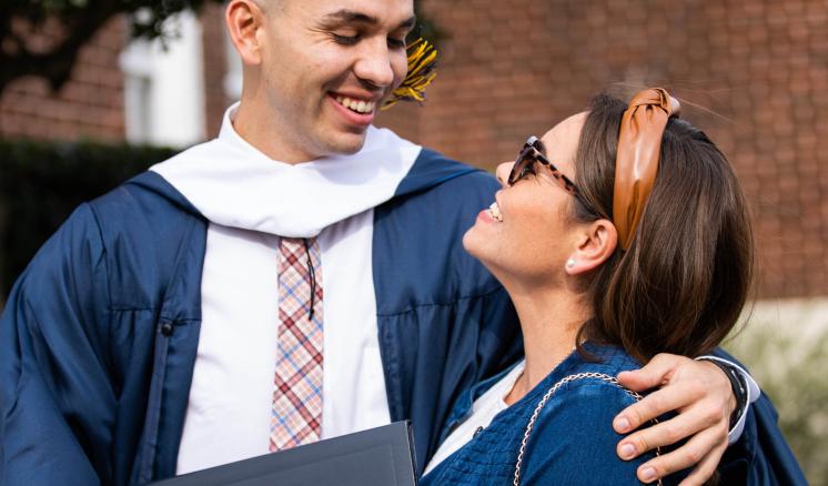 A man in his graduation regalia and a woman looking at each other smiling outside