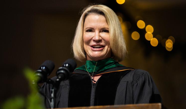 A woman behind a podium smiling with lights behind her head