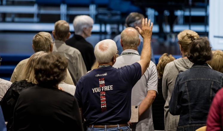  People standing together; an elderly man with his hand raised is in the foreground.