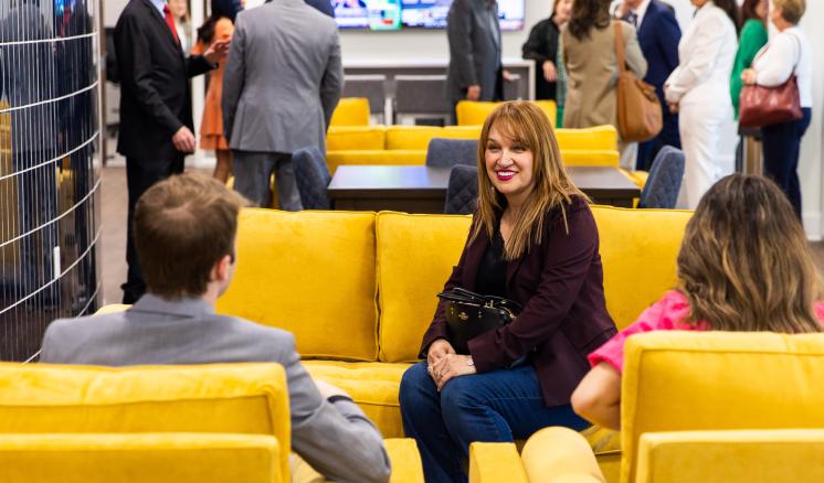 People interacting in a modern room with yellow couches and a large screen.