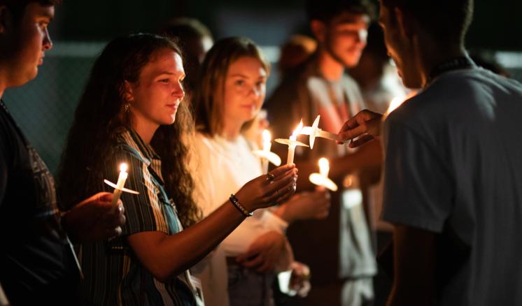 Male and female students lighting candles at event at night