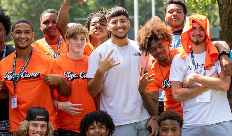 A group of people posing outdoors, some wearing orange shirts, smiling and making hand gestures.