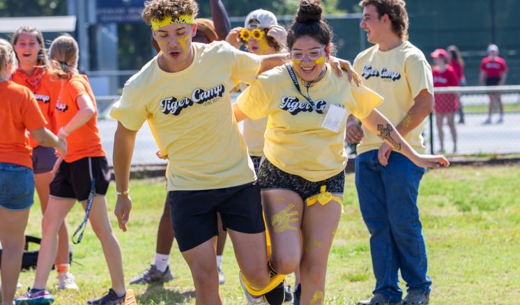 2022_tiger_camp_saturday_tiger_games_0141_web Participants in yellow T-shirts compete in a three-legged race outdoors.