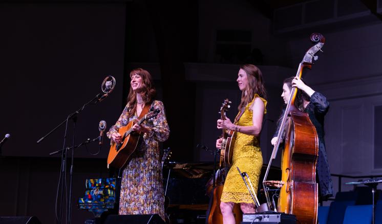 2023_hilltopu_monday_0336 Three female musicians perform on stage with guitars and a double bass.