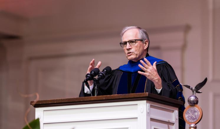 A man in academic regalia speaking behind podium