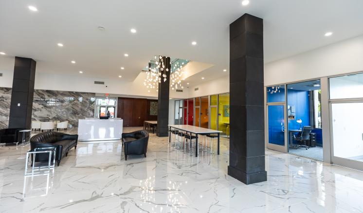  Modern lobby with glossy white marble floor, black leather seating, colorful paneling, and glass-walled office.