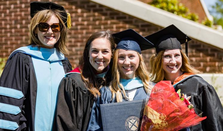 Four people in academic regalia celebrating a graduation outdoors.