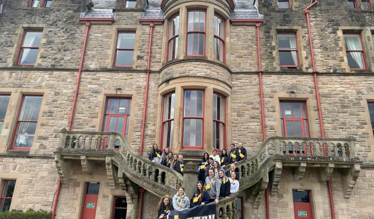 A group of people on stairs in front of a large old stone building holding