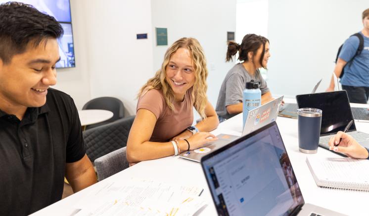 Male and females sitting at desk smiling with eachother with papers and computers on the table