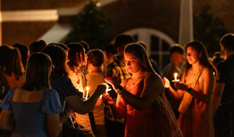 Female students lighting candles at event at night