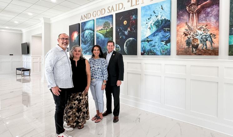 Men and women inside standing in front of paintings 