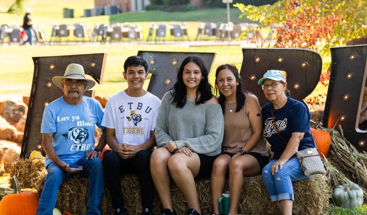 Group of males and females sitting smiling at the camera in front of a ETBU sign