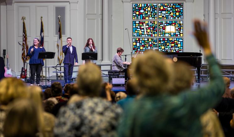 Men and women on stage singing with people worshipping in the foreground in a chapel