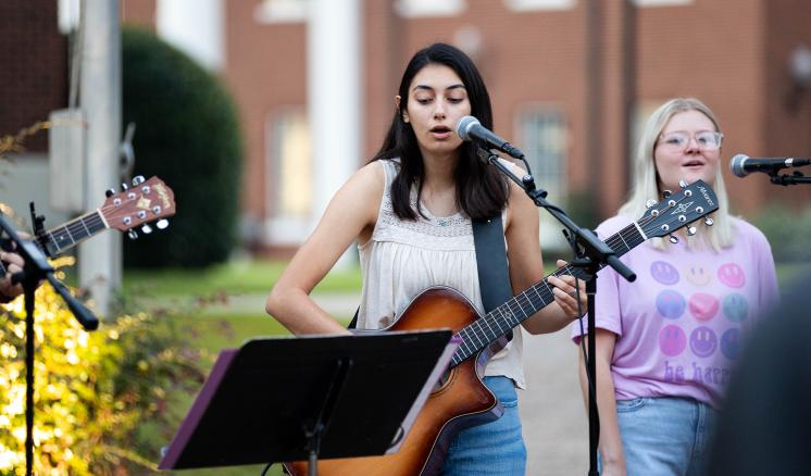 Woman singing and playing guitar with woman singing in the background