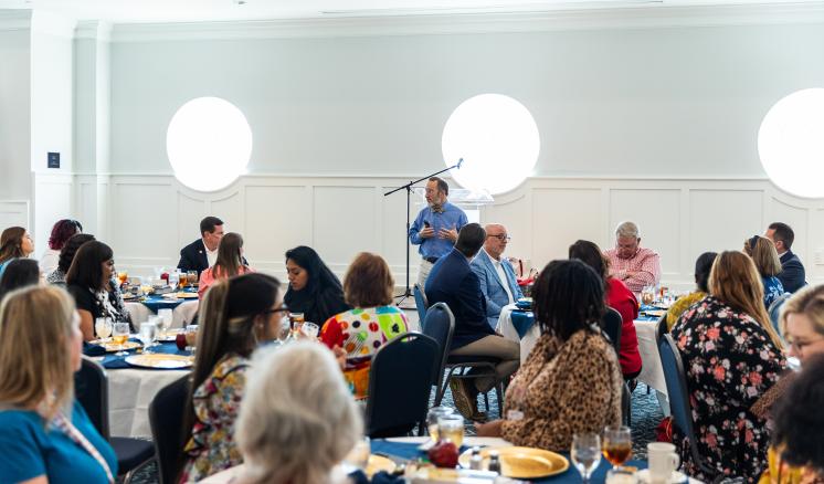 Group of males and females sitting at tables listening to a speaker inside