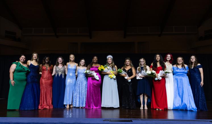 A group of women in ballgowns smiling at the camera on stage