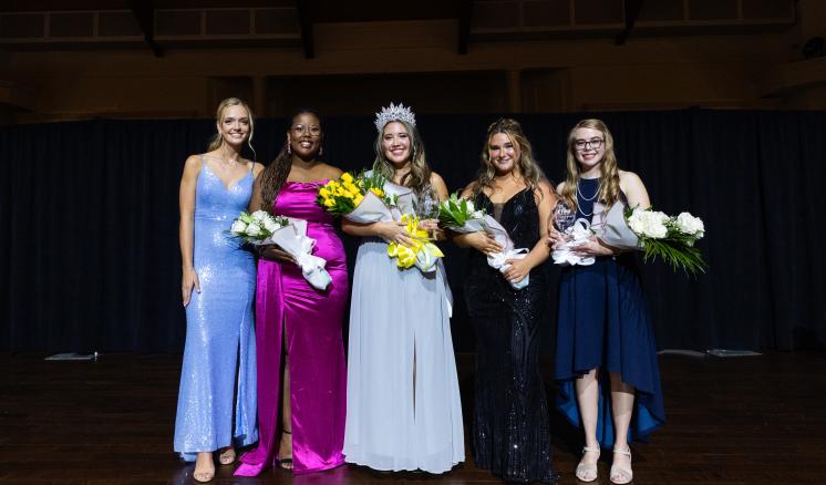 A group of women in ballgowns smiling at the camera on stage