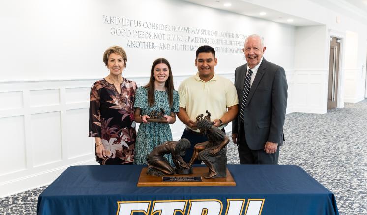 Two males and females standing in front of a table with a navy ETBU tablecloth and Jesus feet washing statue on the top of the table