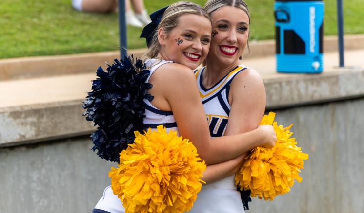 Two female cheerleaders hugging and smiling.