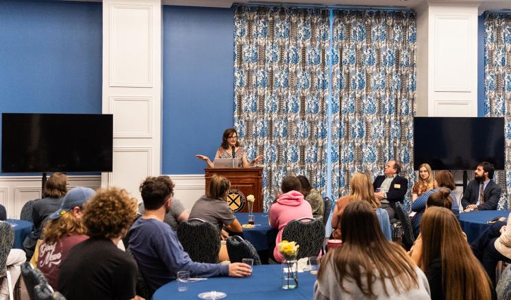 A woman speaking behind a podium to a room full of people.