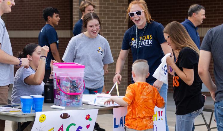 A group of male and women students with a kid smiling at a table with candy and posters