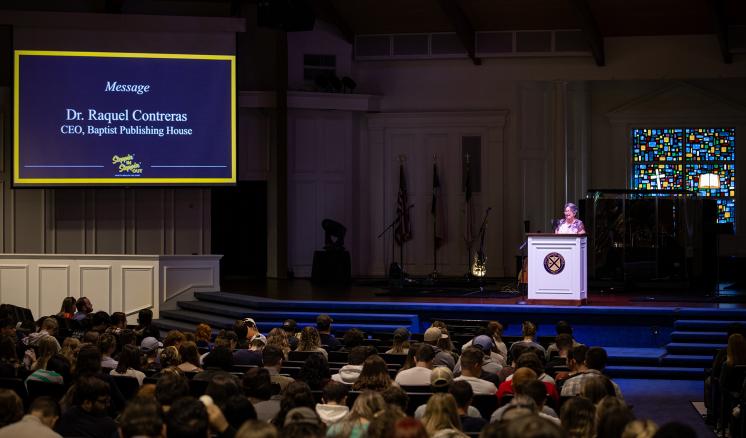 Woman speaking on a stage behind podium in front of a crowd.