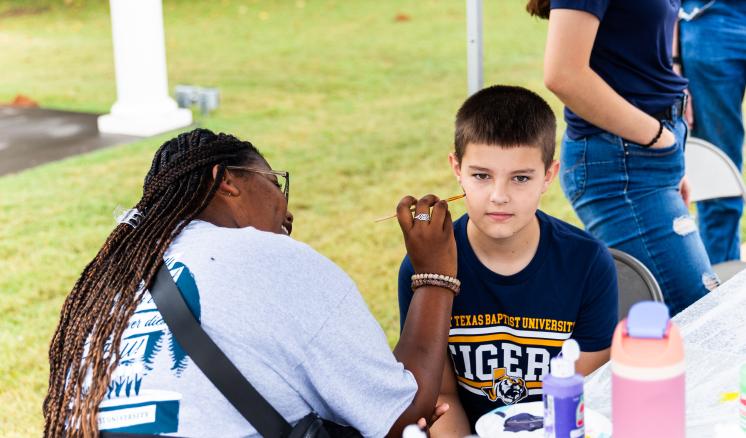  A person applies face paint to a young boy at an outdoor event.