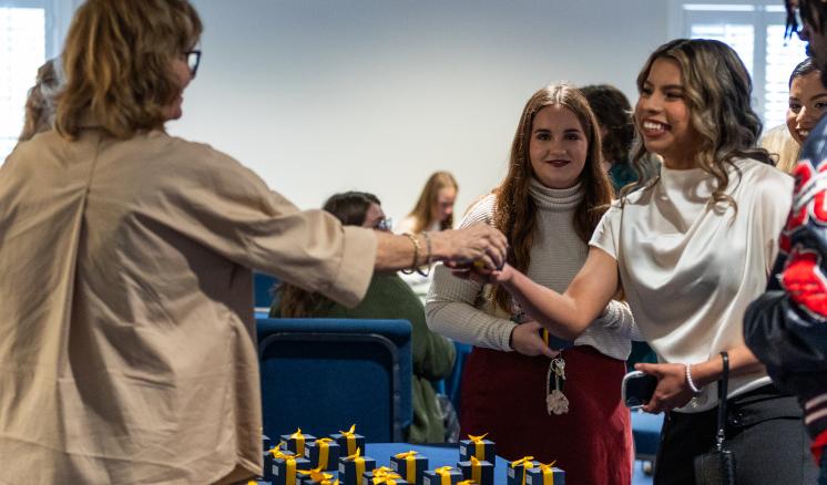 Woman handing a smiling female student her graduation ring box 