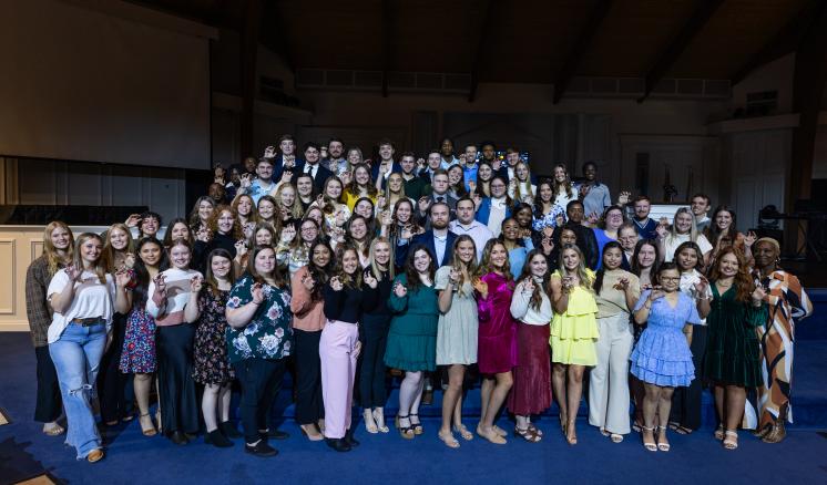 Large group of male and female students holding their graduation rings smiling at the camera 