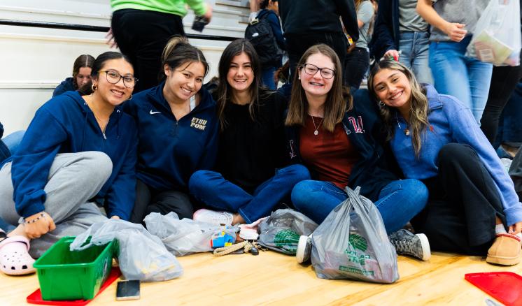 Group of female students sitting on the floor in gymasium smiling a the camera